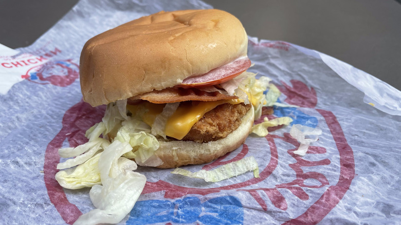 A chicken patty with bacon, lettuce, tomato, and cheese sits on a Wendy's wrapper.