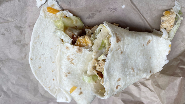 A chicken wrap split in two sits on a piece of paper it was wrapped in.