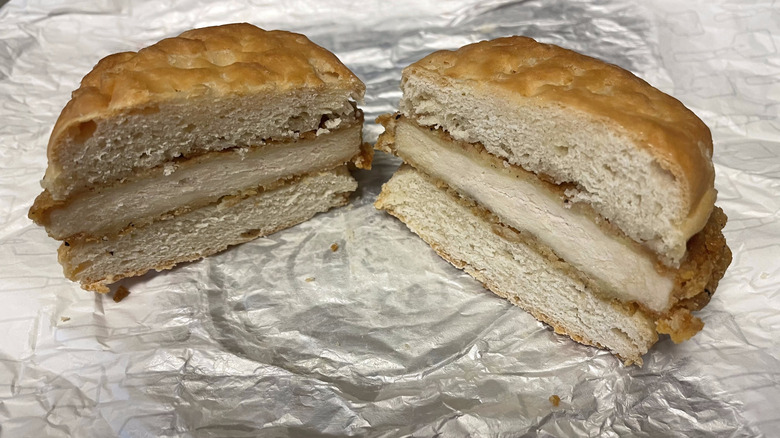 Two halves of a chicken on a biscuit sandwich sit on a piece of foil wrapper.