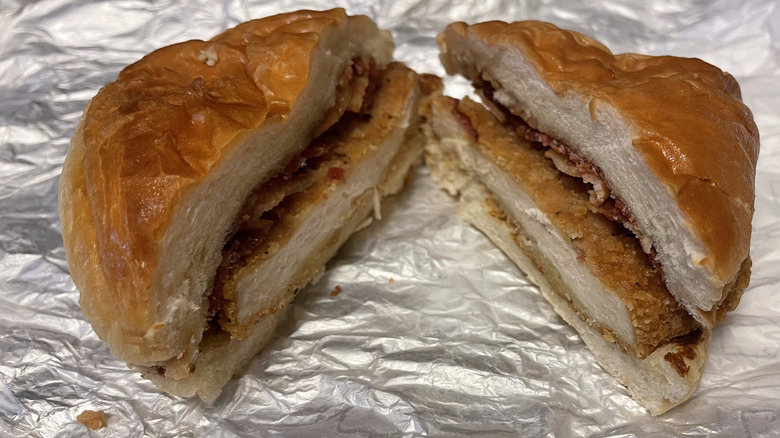 Two halves of a chicken sandwich with bacon on a croissant bun sit on a foil wrapper.