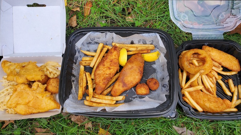 Takeout containers of fish and chips from three restaurants on grass