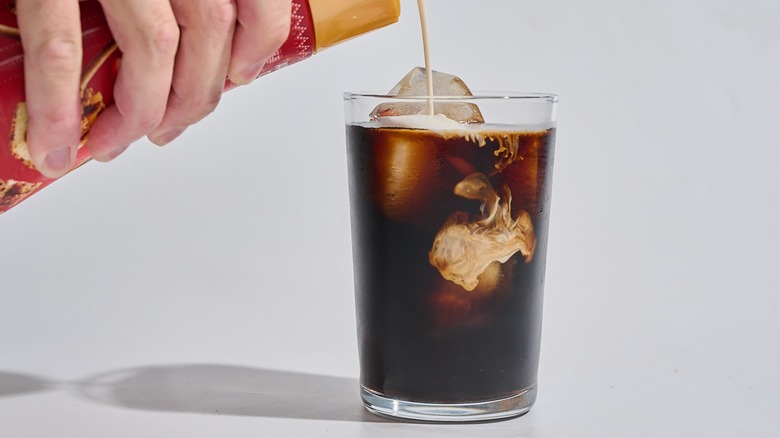 Hand pouring creamer into iced coffee