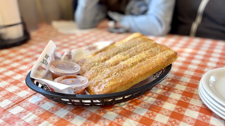 Pizza Hut breadsticks in a basket with two pots of sauce on a checkered tablecloth