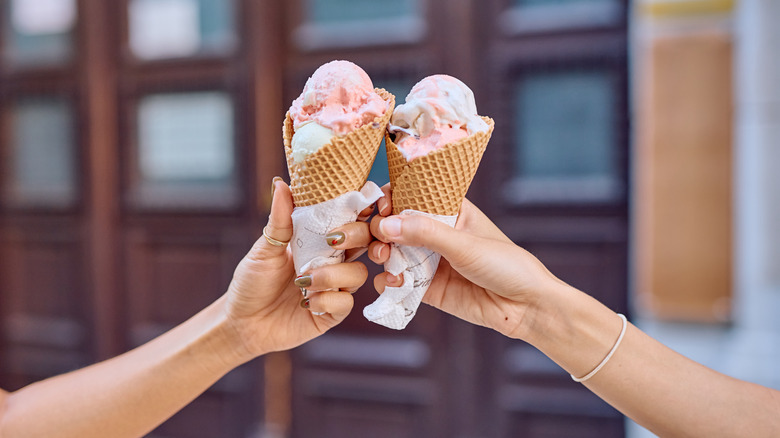 Two arms holding up ice cream cones.