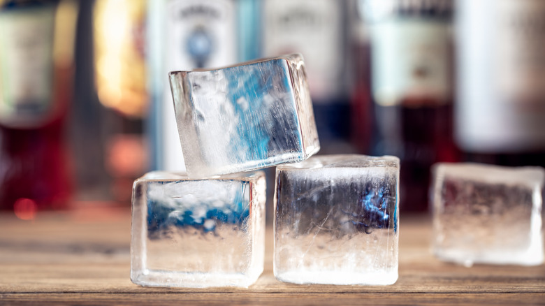 Clear ice cubes on bar counter with liquor bottles blurred in the background