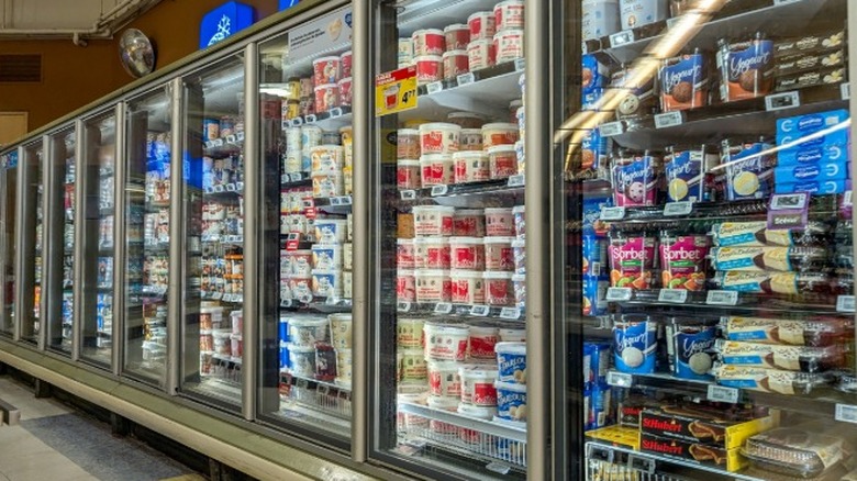 The ice cream aisle of a grocery store with different kinds of ice cream and other frozen treats stocked on refrigerator shelves.