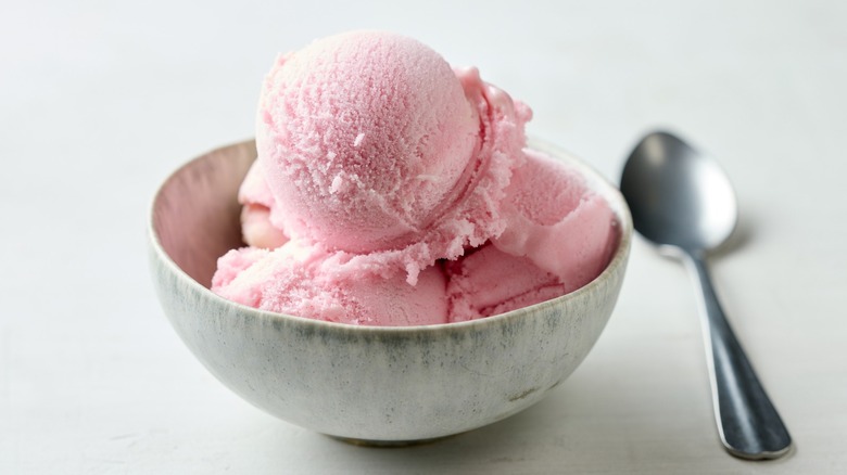 A bowl of low-fat strawberry ice cream sitting on a countertop next to a spoon.