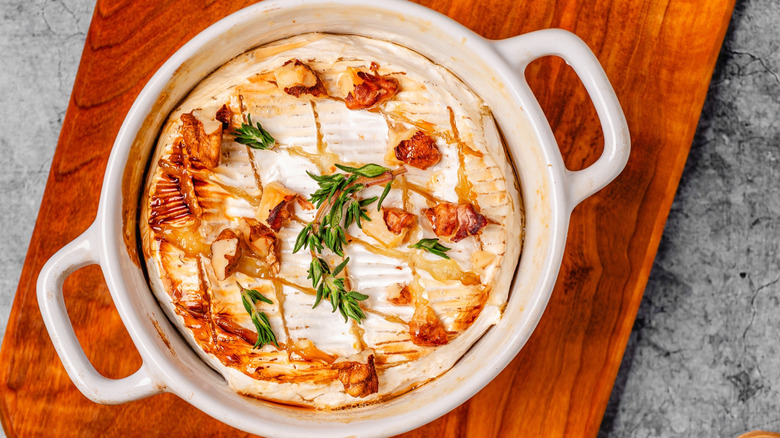 A dish of baked brie topped with pecans, honey, and rosemary