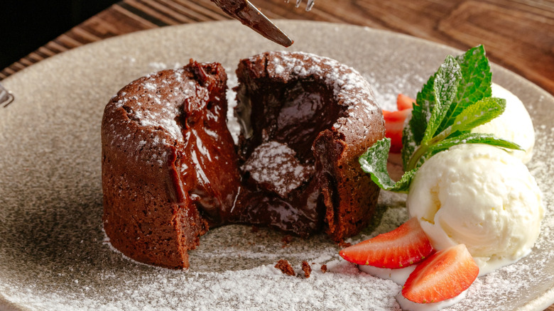 A split-open molten lava cake with a side of strawberries and ice cream