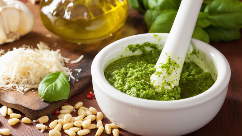 Pesto is prepared with basil, cheese, and pine nuts in a mortar and pestle