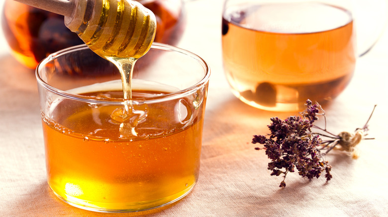 Honey is warmly lit in glass bowls with dried herbs in the frame