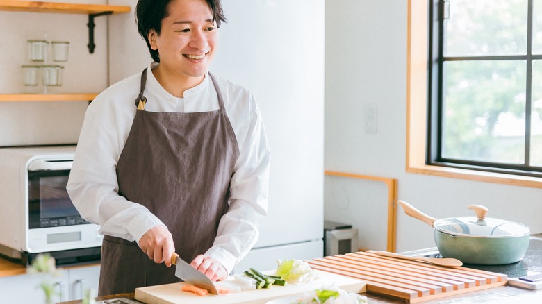 A man smiling in the kitchen while chopping veggies
