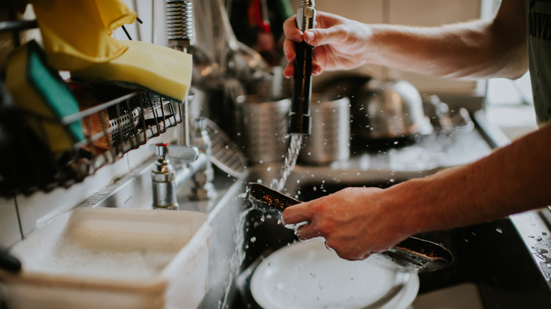A person washing dishes in a sink equipped with a pull-down faucet