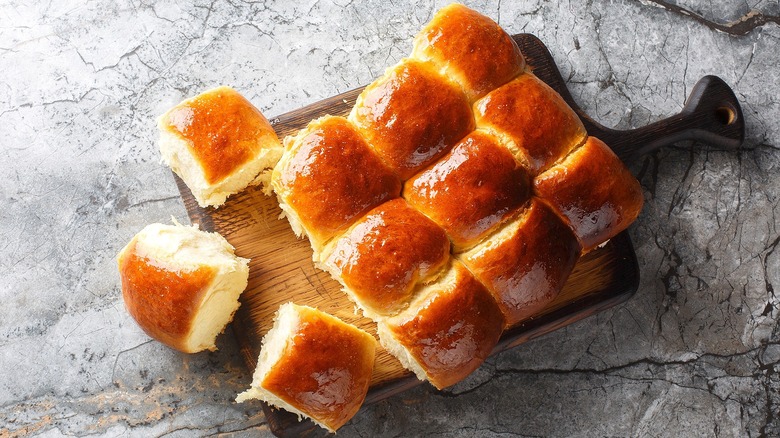 Fresh-baked Hawaiian rolls on a wooden serving board over a gray surface.