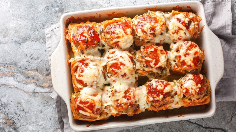 Meatball-stuffed bread rolls topped with tomato sauce and melted cheese in a white casserole dish.