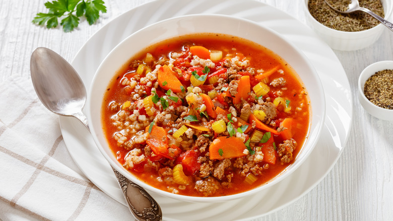 A bowl of hamburger soup on a white wooden table.