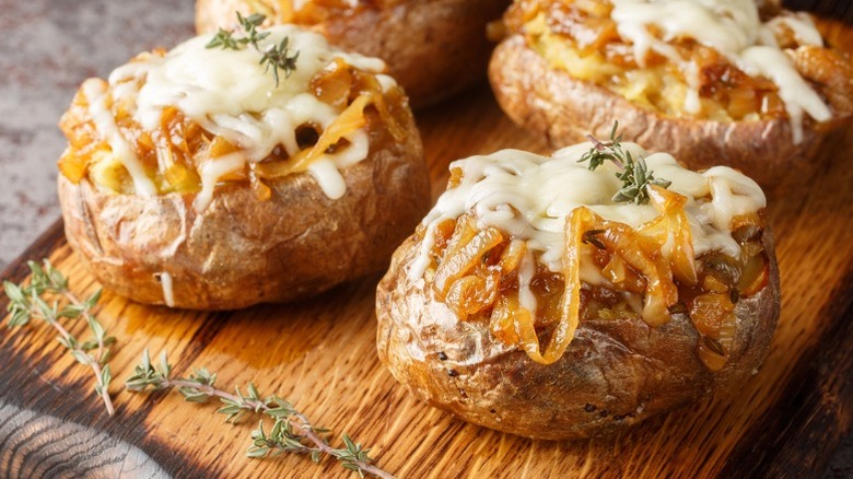 French onion baked potatoes with cheese on cutting board.