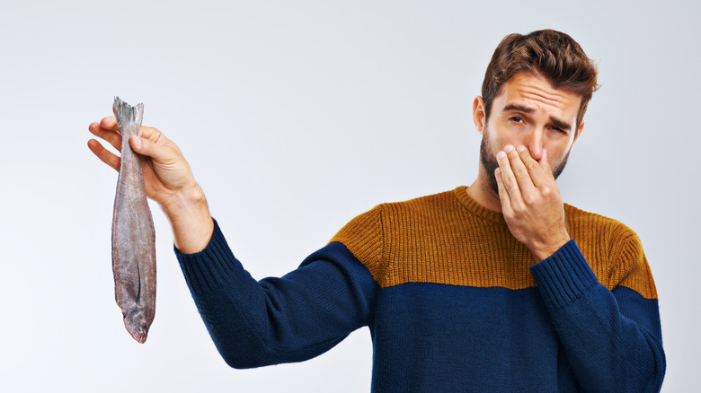 Man holding a stinky fish and holding his nose