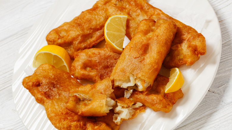 Crispy, beer-battered fish on a white plate with lemon wedges