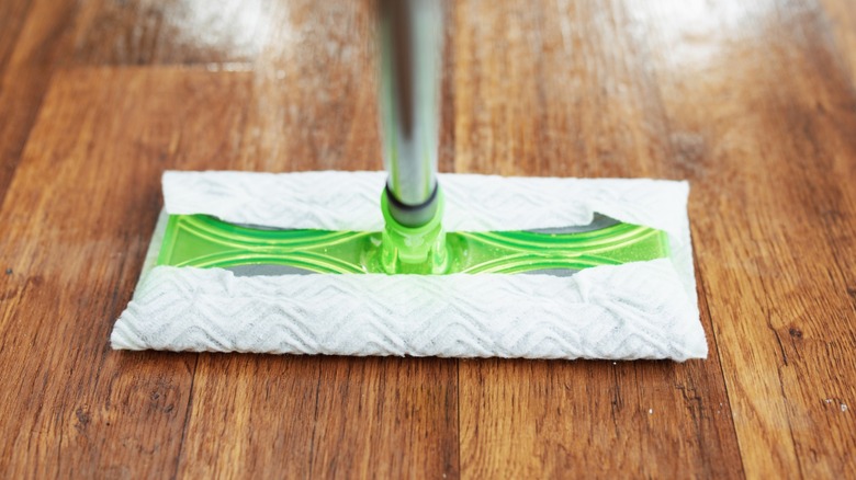 A Swiffer Sweeper mop being used on a wood kitchen floor.