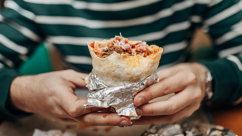 Person holding a half-eaten burrito wrapped in aluminum foil