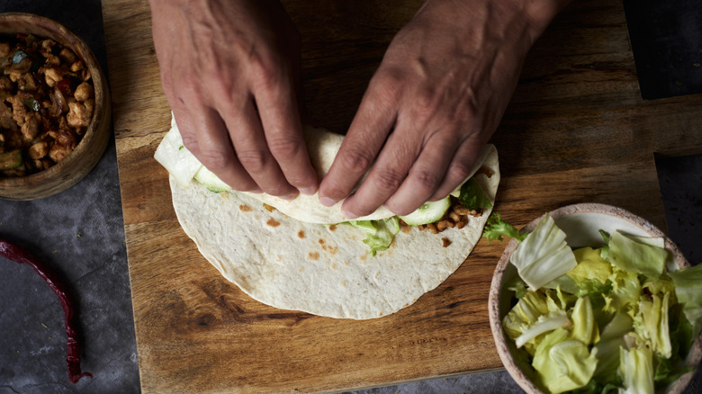 Person rolling a burrito on a wooden cutting board