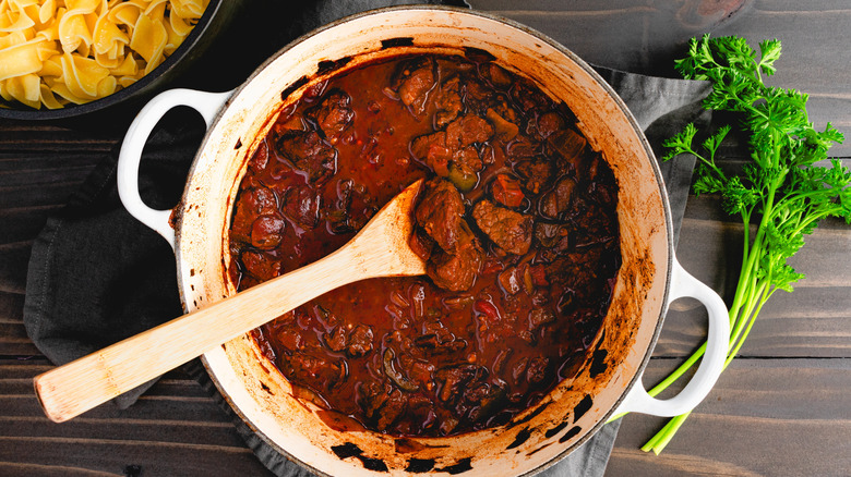 Goulash simmering in an enamel Dutch oven with a wooden spoon.
