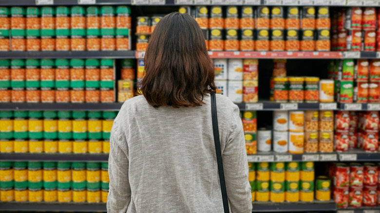 Woman staring at store shelf of canned veggies