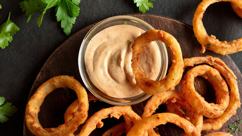 Close up view of deep fried onion rings on wooden serving dish on a dark background