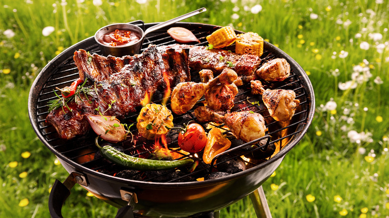 Meats and vegetables on a grill that's placed over grass