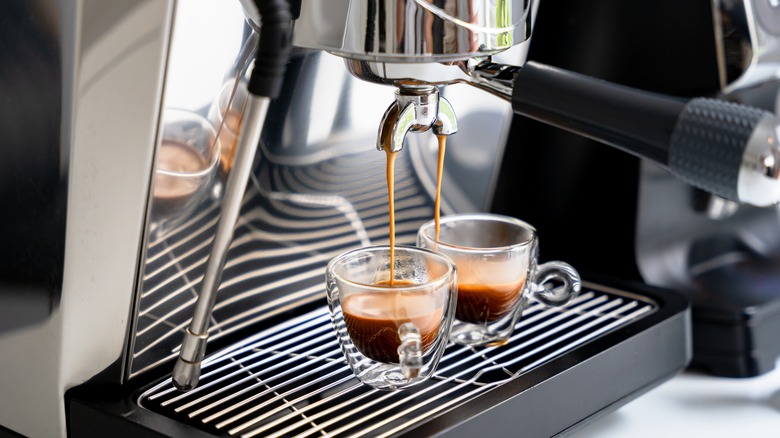 Brewing espresso in to glass cups silver coffee espresso machine white and clean interior.
