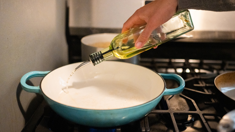 Man pouring oil into ceramic pan on stovetop.