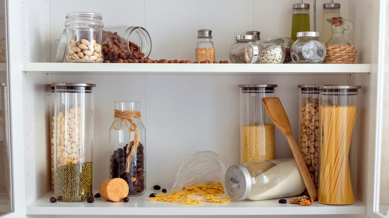 interior of a cluttered kitchen cabinet with grains, oils, nuts, and noodles.