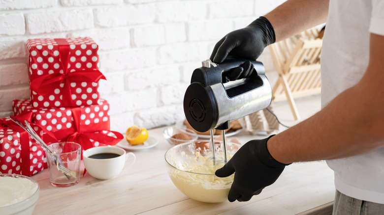 Person mixing up Bisquick in a glass mixing bowl with a handheld electric mixer