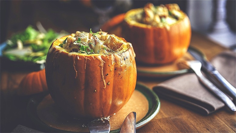 Two small stuffed pumpkins with fresh greens and melted cheese on tan plates with dark green trim