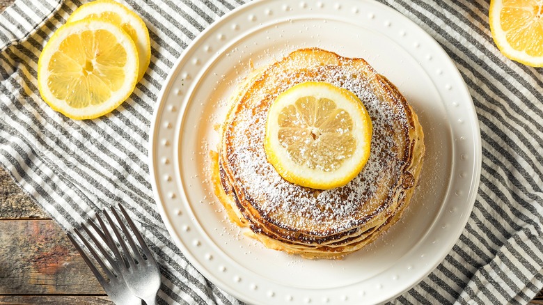 Top-down view of lemon ricotta pancakes topped with fresh lemon slices on a white plate over a gray and white dish cloth