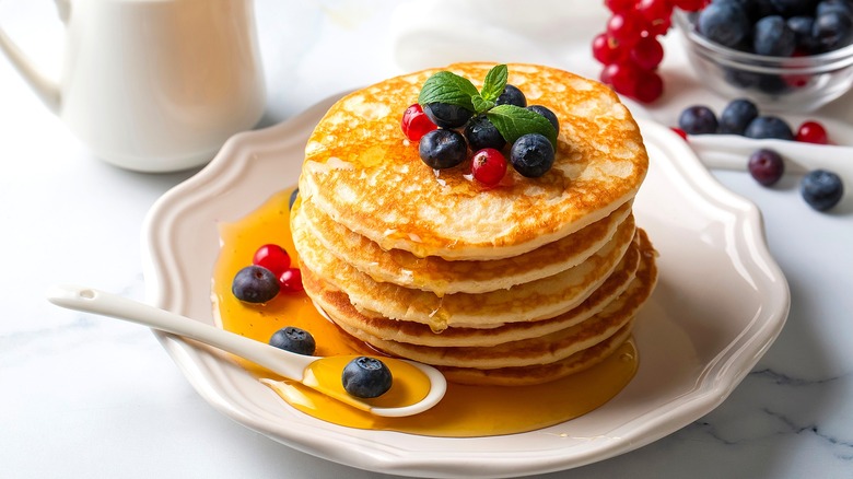 Stack of pancakes with mixed berries and maple syrup on a white scalloped plate