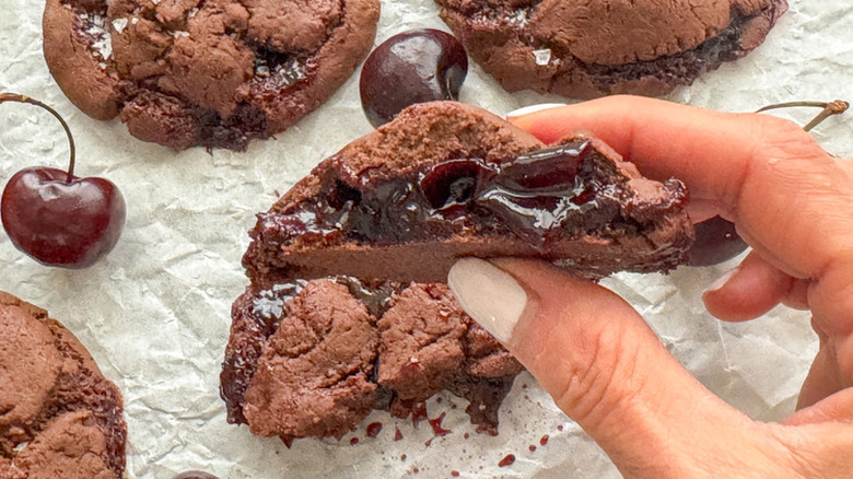 A hand holding a bitten a chocolate cherry-stuffed cookie.