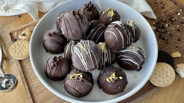 A bowl of chocolate-covered ice cream bites alongside some crumbled cookies.