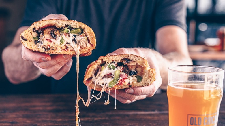 A person holding two halves of a calzone at Old Chicago Pizza & Taproom