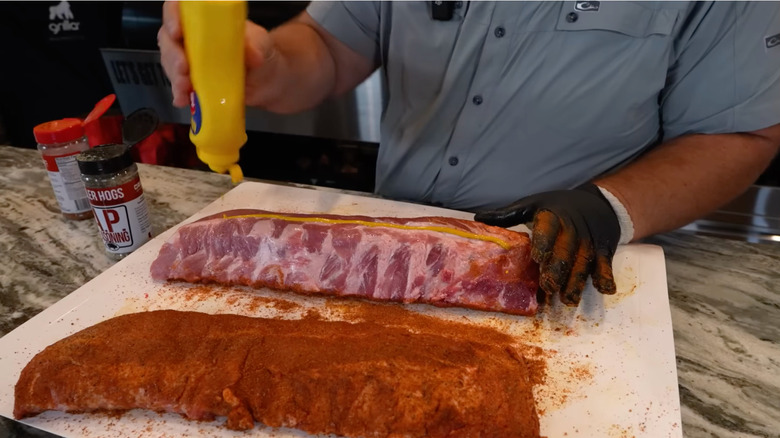 Adding yellow mustard to baby back ribs before dry rub