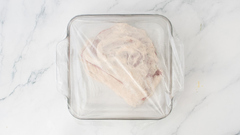 A square casserole dish wrapped in plastic with a marinated steak