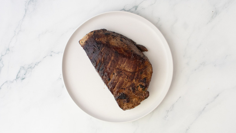 A seared steak resting on a white plate