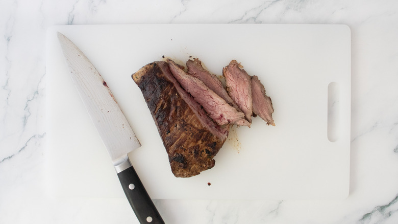 A seared steak being sliced on a white cutting board