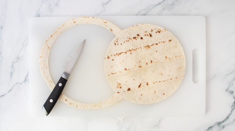 A flour tortilla on a cutting board with about 1-inch removed from the edges