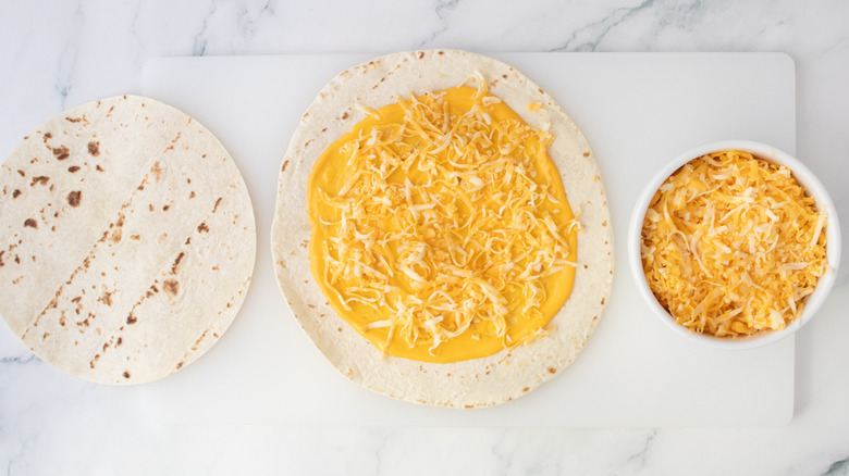 A large flour tortilla with nacho cheese sauce and shredded cheese