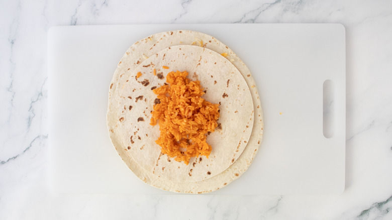 A portion of red rice on top of a stack of tortillas