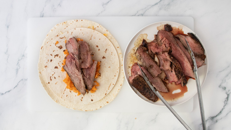Slices of steak and red rice on a stack of tortillas