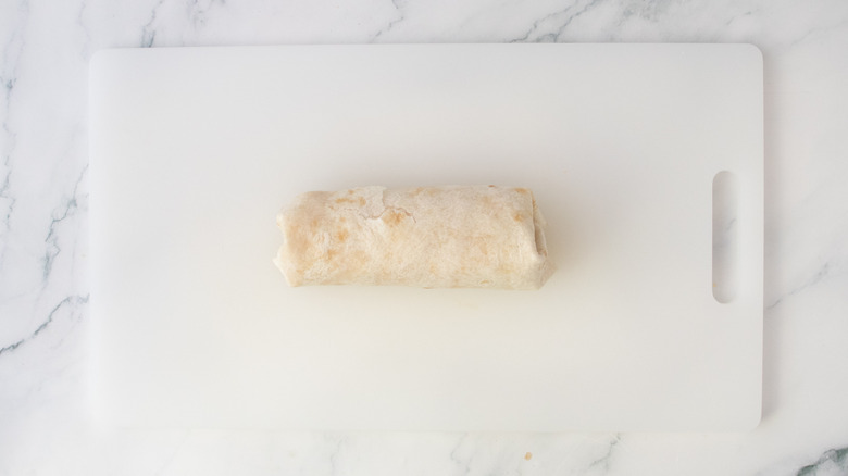 A tightly rolled burrito on a white cutting board