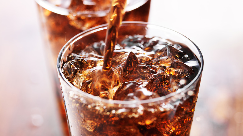 Soda being poured into drinking glass filled with ice.